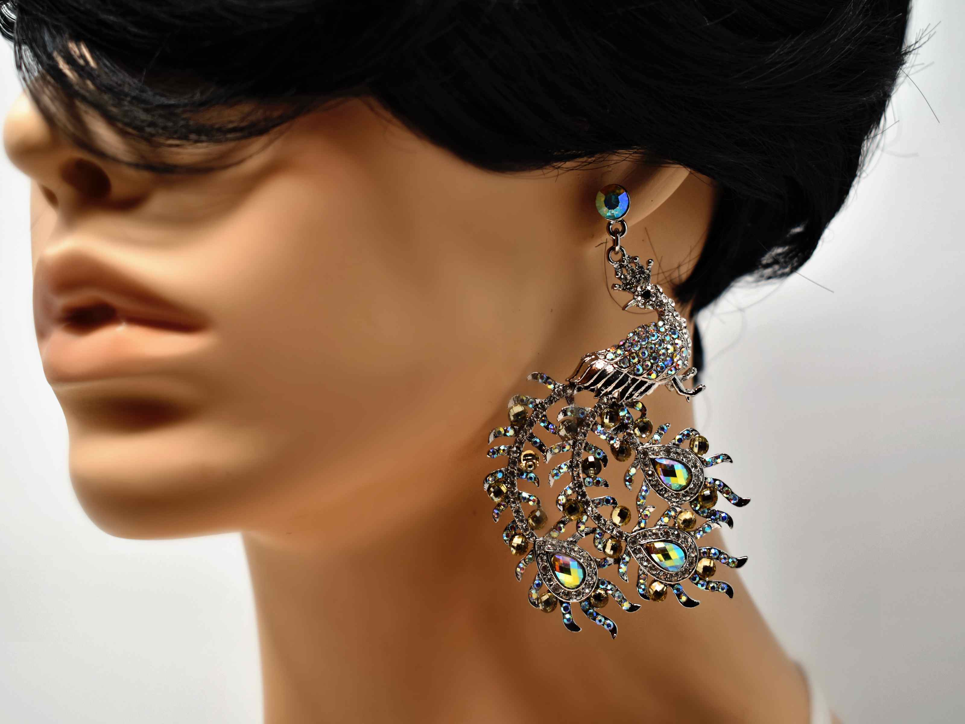 How about our Hebe statement formal peacock dangle drop earrings. These earrings are silver with stones all over. It also has a push back clasp and is 3 inches in Length.