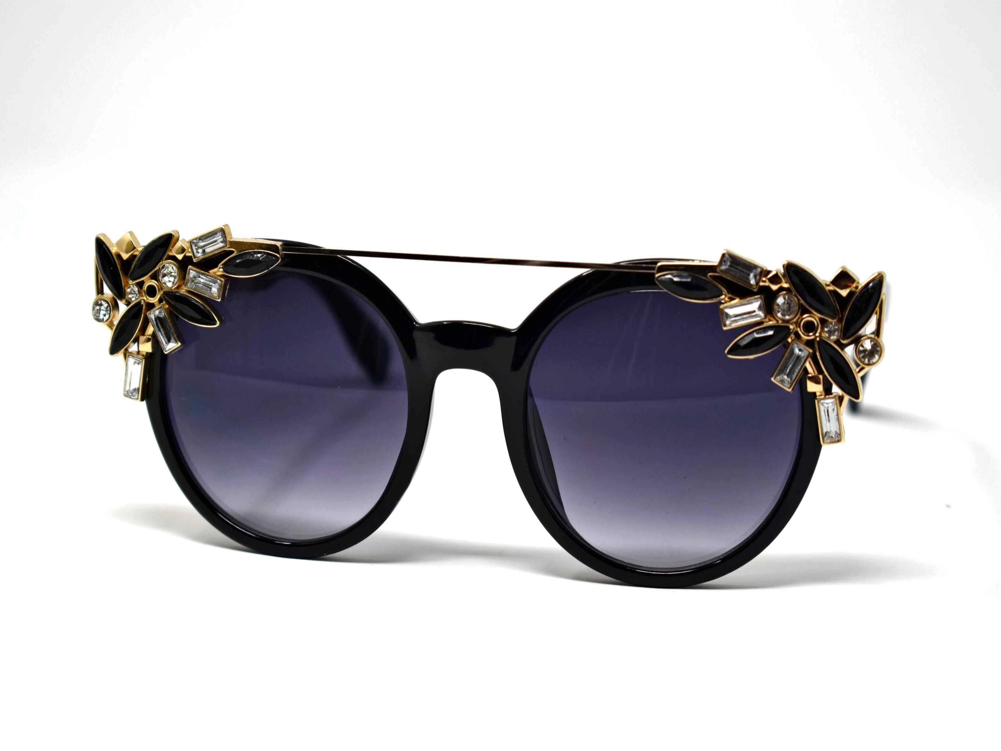 Trend setter and attention getter is what they will call you in these Pansy Black sunglasses with a sleek gold trim adorned in clear and black gems, in a pantos style frame.