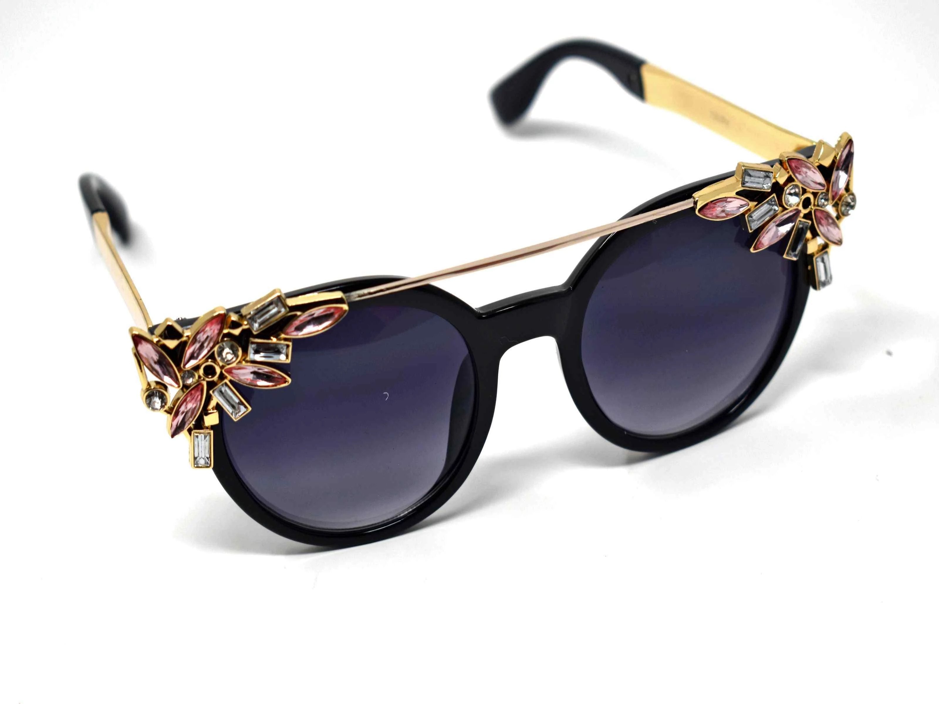 Trend setter and attention getter is what they will call you in these Pansy black sunglasses with a sleek gold trim adorned in pink and clear gems, in a pantos style frame.